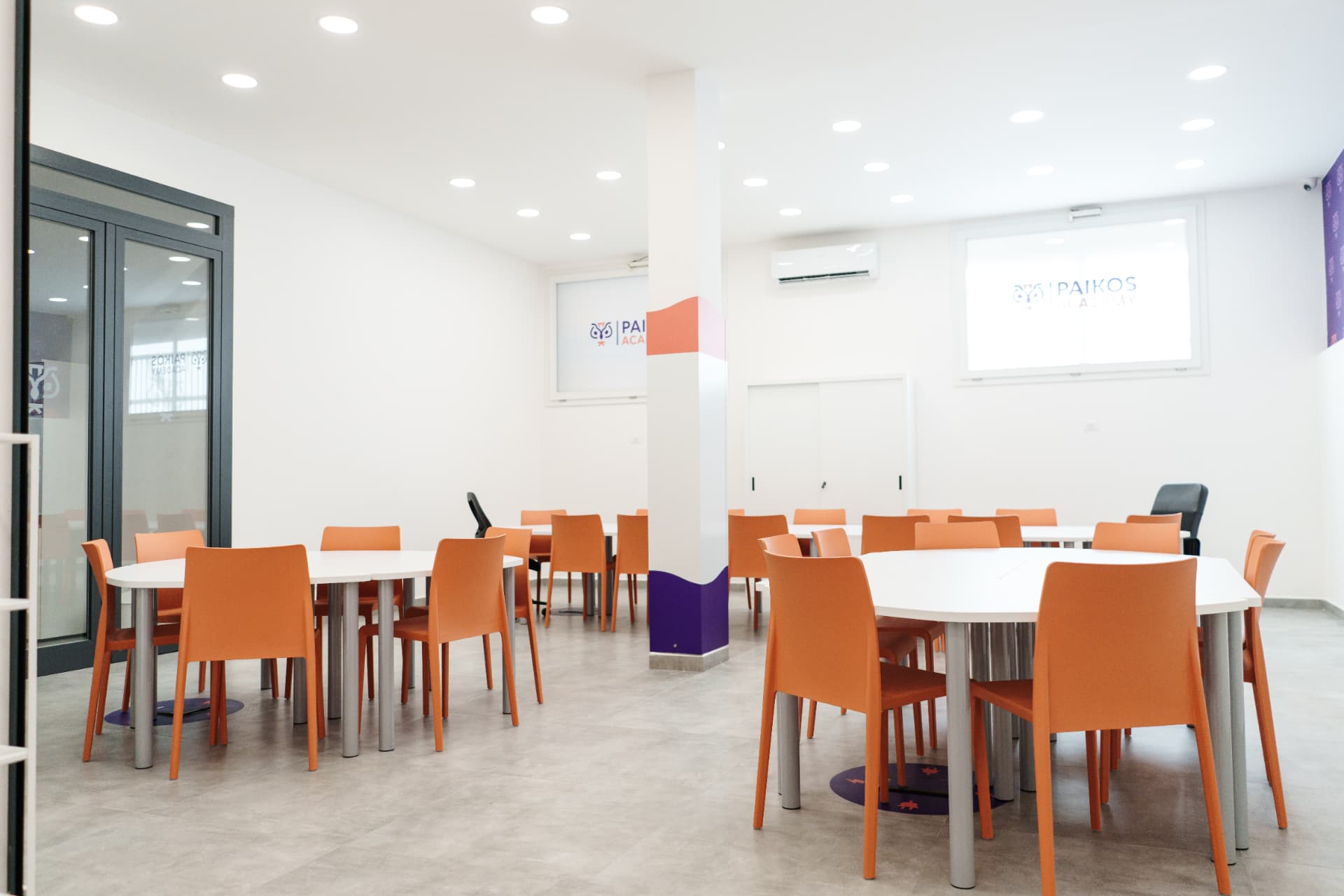 Grande aula studio di Paikos Academy con tavoli bianchi, sedie arancioni e schermi